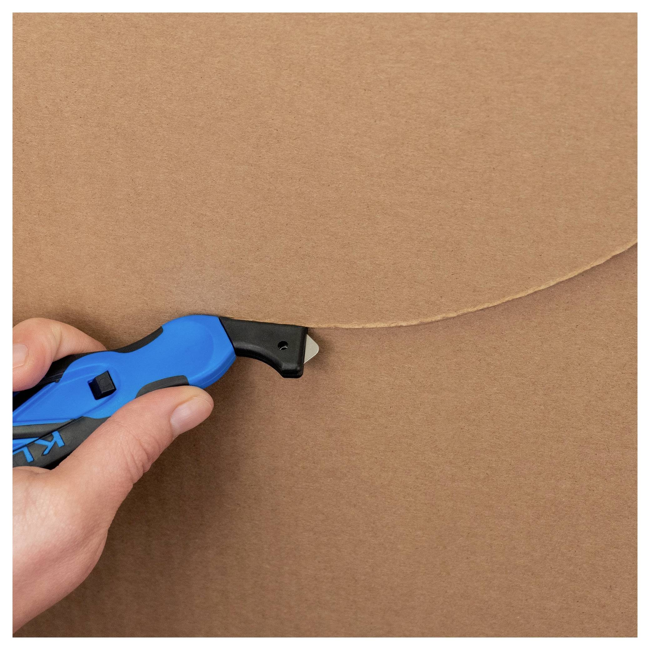 Hand using a blue utility knife to cut along a seam in brown cardboard.