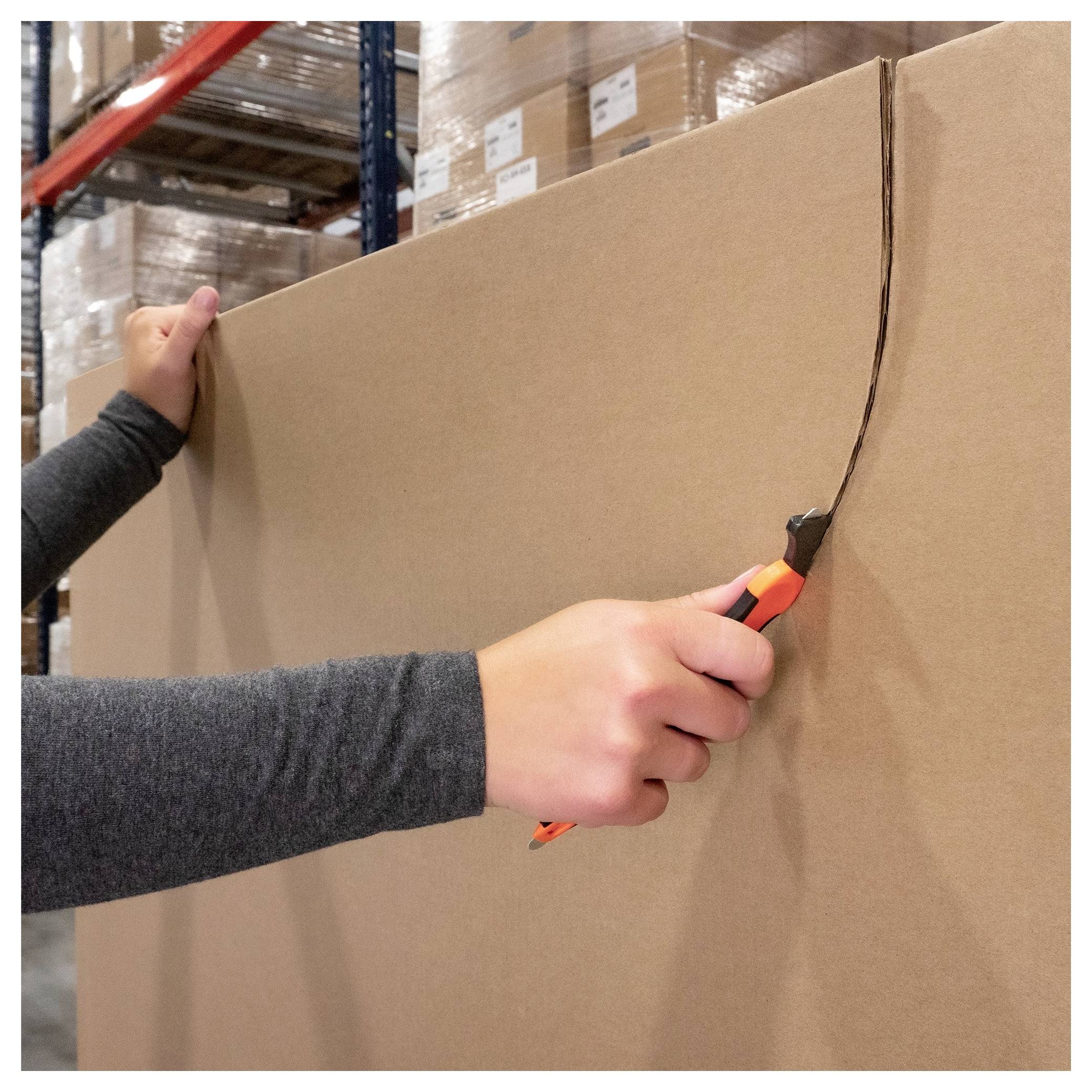 A person uses a box cutter to cut open a large cardboard box in a warehouse.