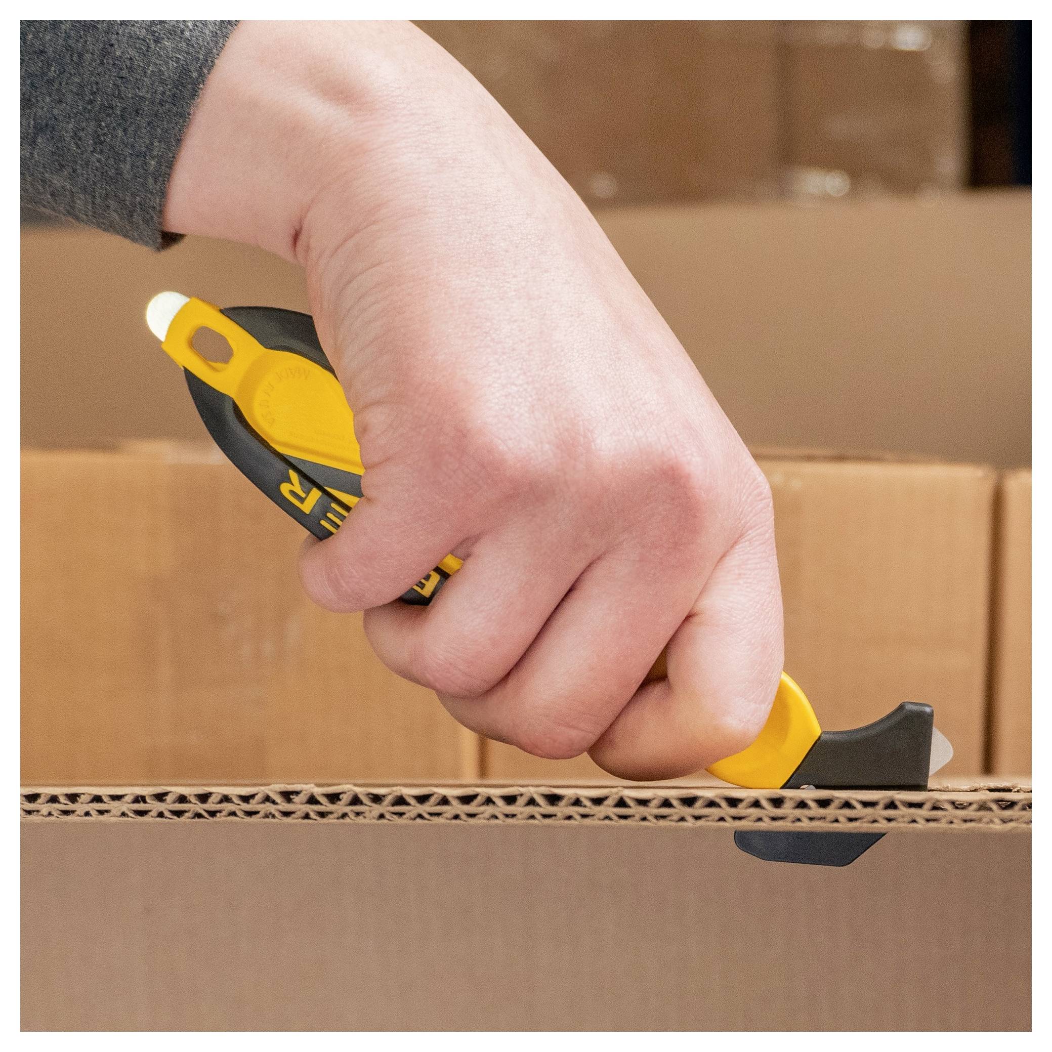 Hand using a box cutter to open a sealed cardboard shipping box.<br>