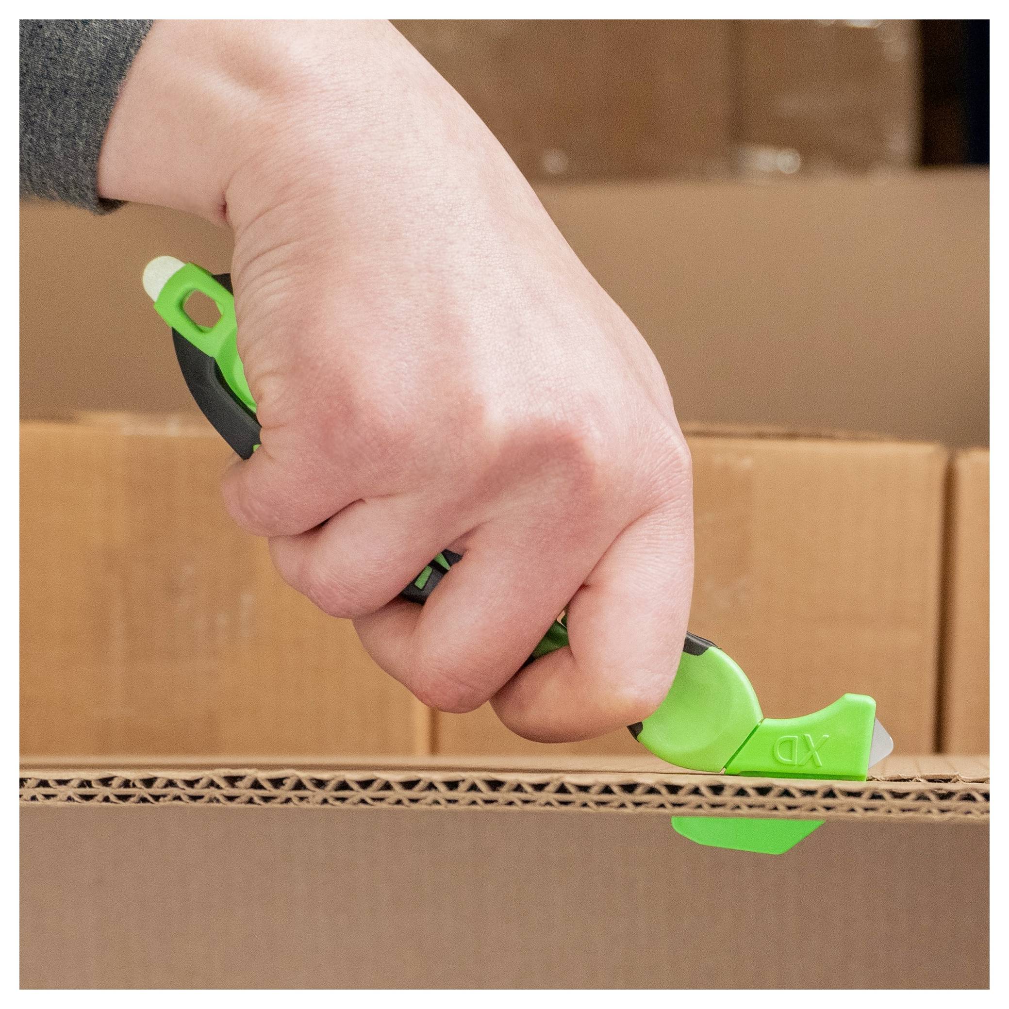 Hand using a green box cutter to slice open cardboard packaging during unpacking.