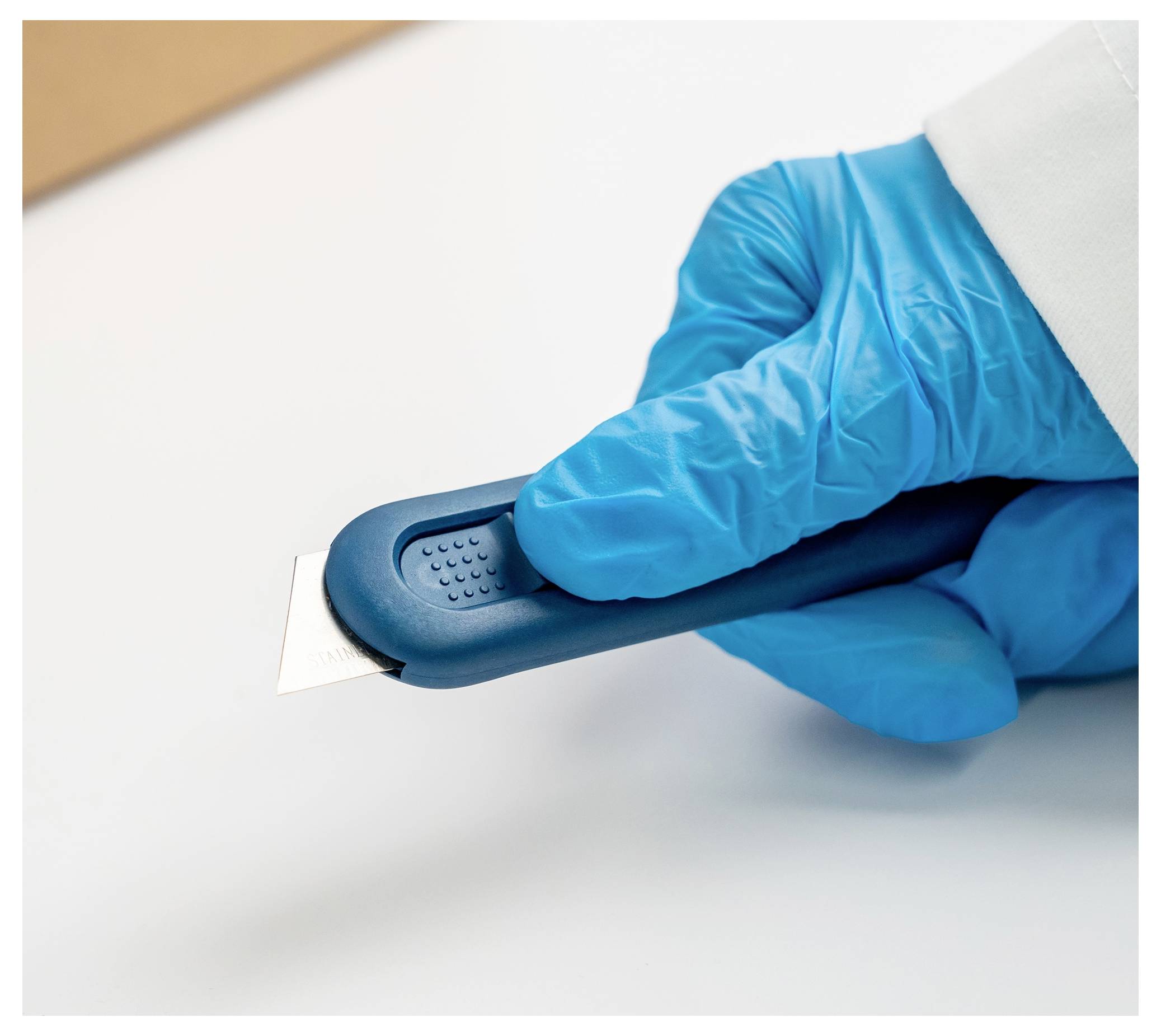Blue-gloved hand holding a retractable utility knife with the blade extended against a white surface.