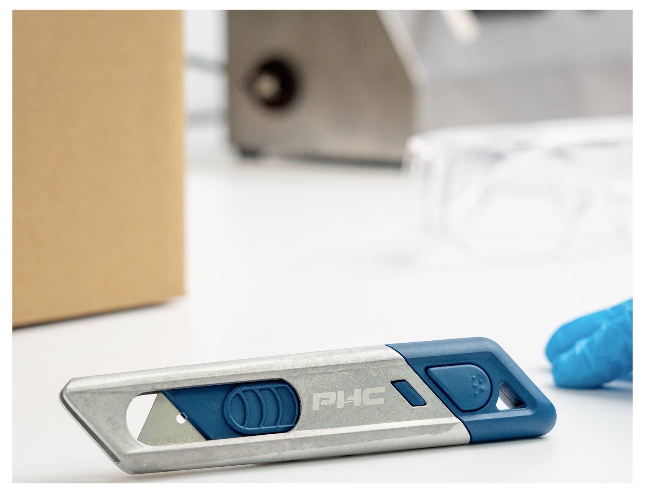 Blue and silver retractable utility knife on a white work surface, with a gloved hand in the background.