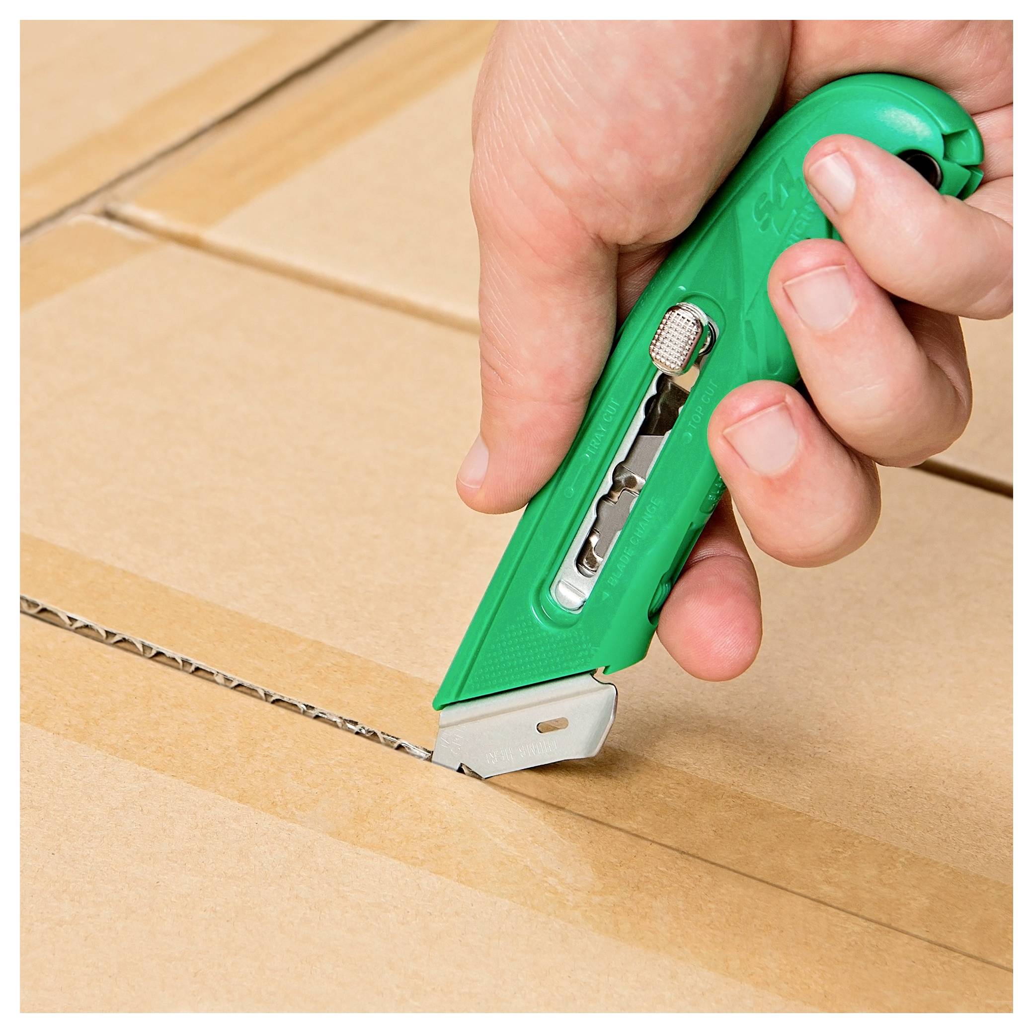 Hand cutting open a sealed cardboard box with a green utility knife.