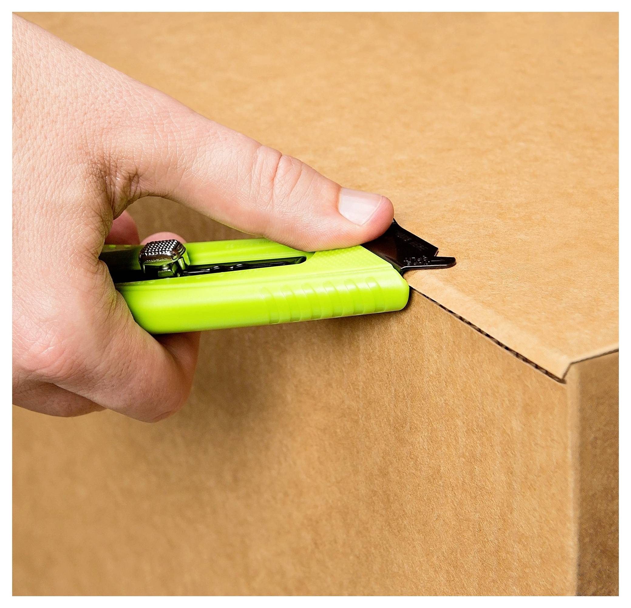 Hand using a green utility knife to cut open a cardboard box.
