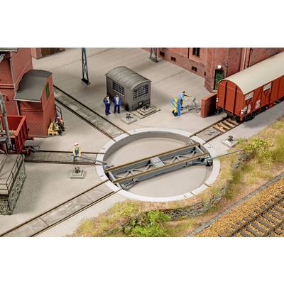 Model train roundhouse and turntable yard with workers, a red freight car, and tracks radiating from the central turntable.<br>