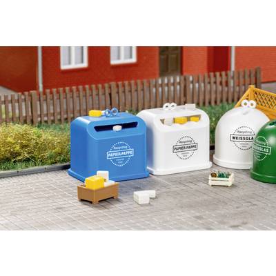 Miniature recycling bins labeled 'Papier-Pappe', 'Papier-Pappe', 'Weissglas' and 'Grünglas' with small sorted trash pieces on a paved street by a fence and building.