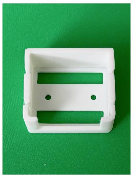 White plastic buckle or clip component on a green background, shown front-on.