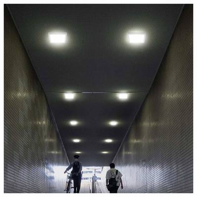 Police officer walking a bicycle through a tiled underground passage, with a person ahead near the bright exit.