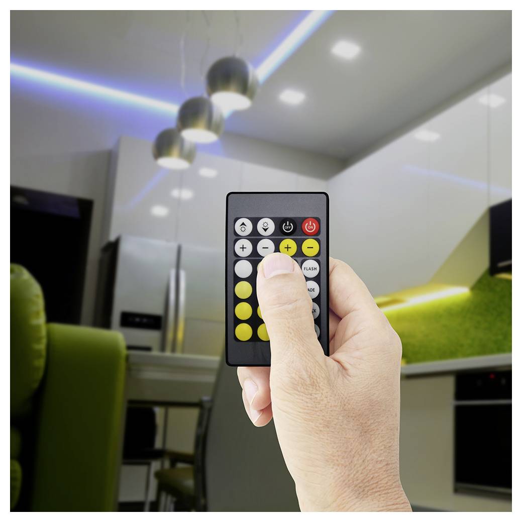 Hand holding a remote control aimed at a ceiling light, with colored light strips visible in a modern kitchen.
