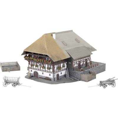 Scale model of a traditional farmhouse with a thatched roof, flower boxes, fenced yard, and small farm carts beside it on a white background.