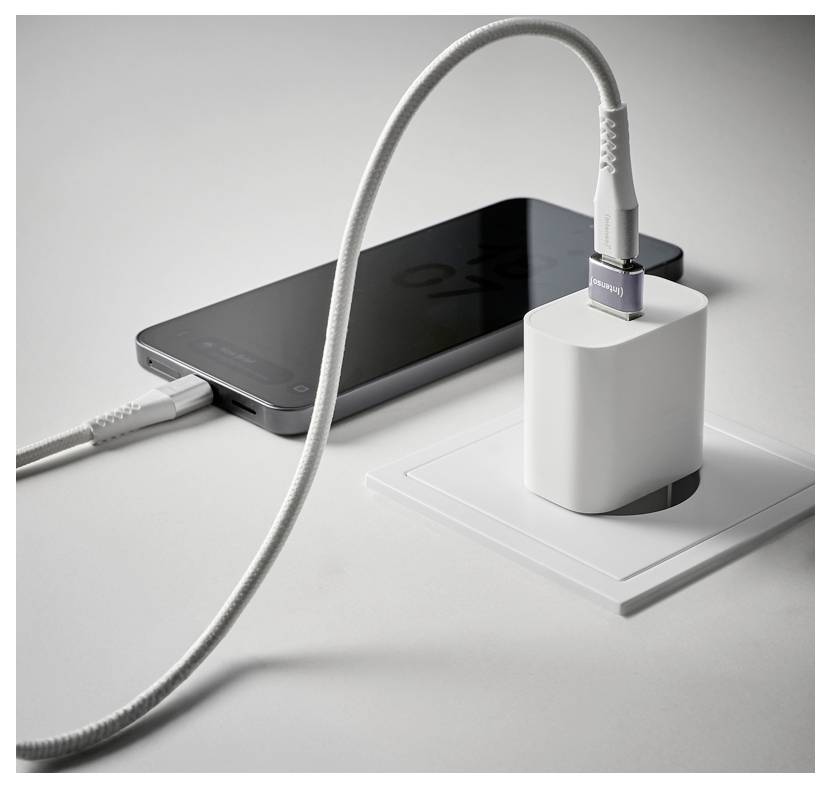 A smartphone is charging with two white cables connected to a wall outlet adapter on a white surface.