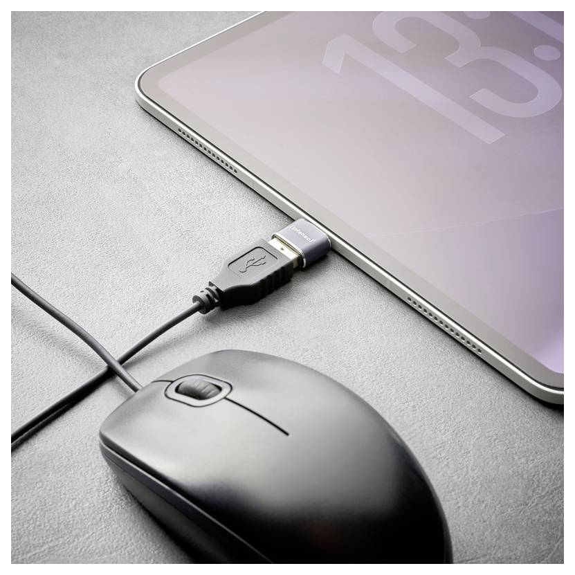 Tablet connected by USB cable beside a black wired mouse on a gray surface, suggesting device charging or data transfer.