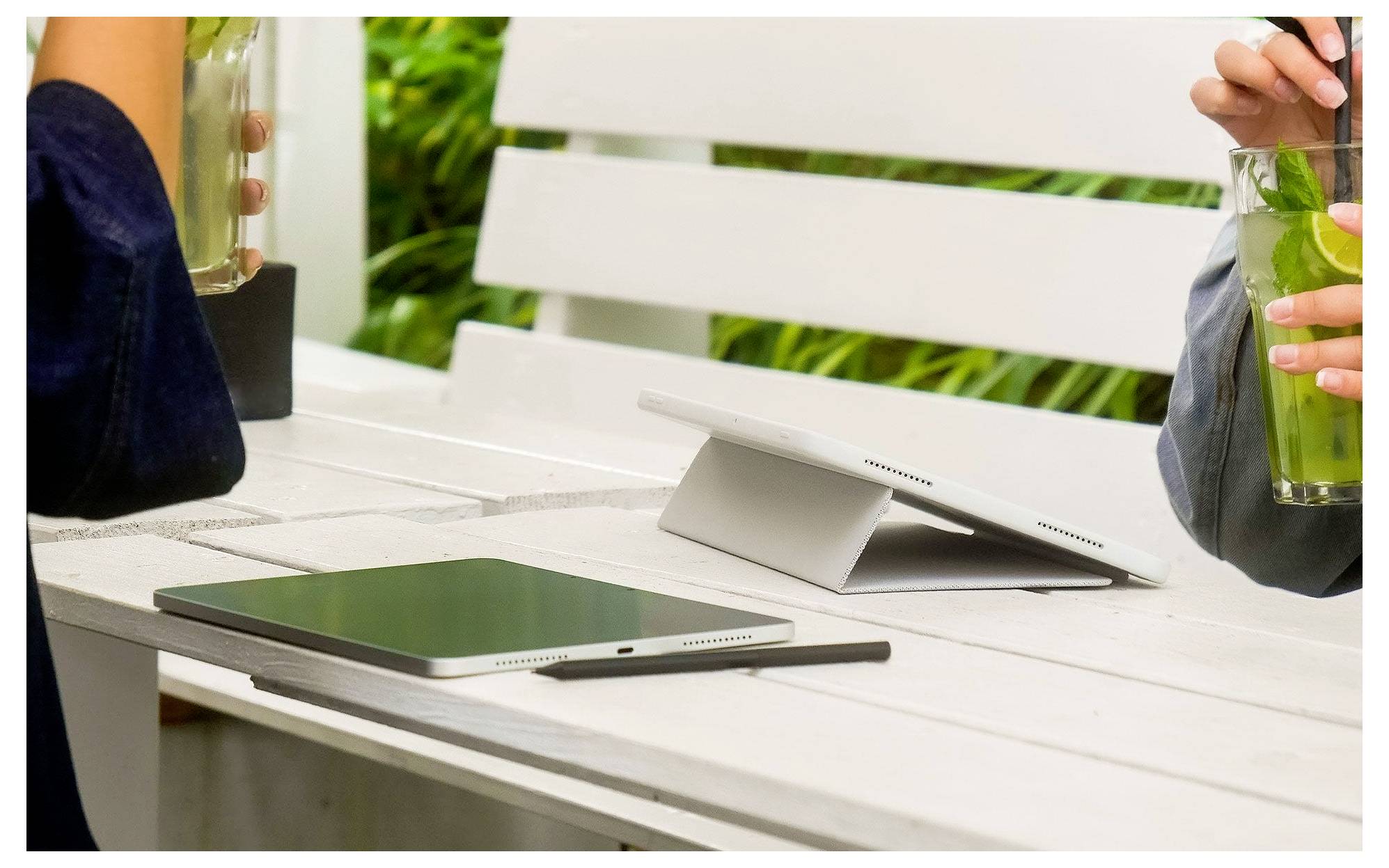 Tablet and smartphone on a white outdoor table, with people holding drinks in the background.