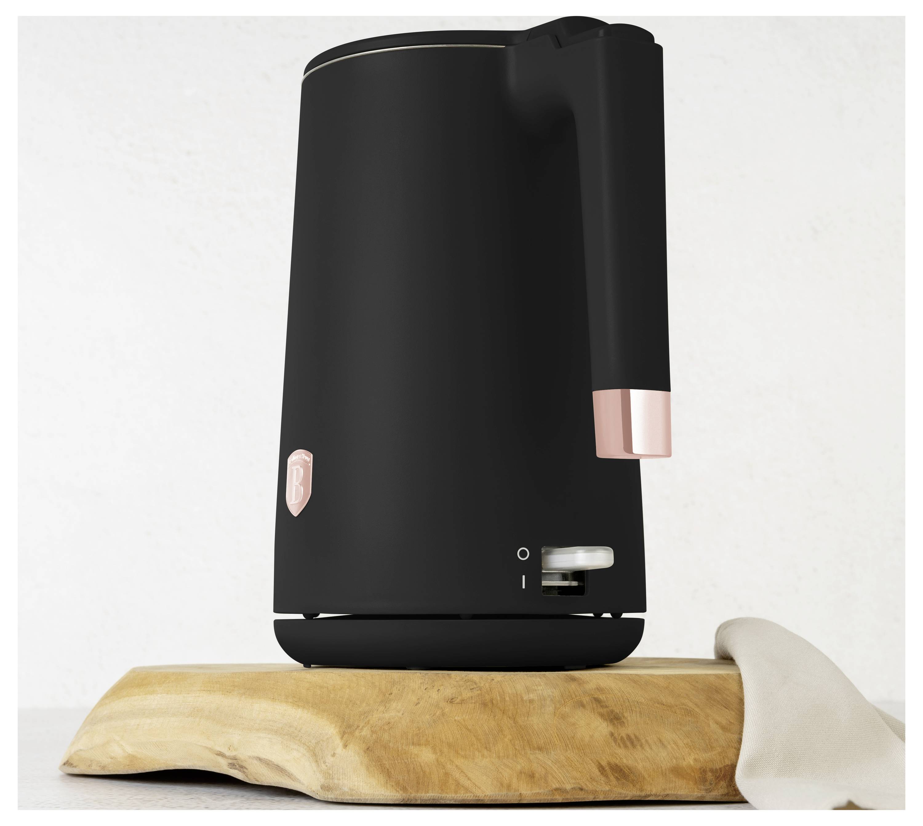 Black countertop electric kettle with rose-gold accents sitting on a wooden cutting board against a plain wall.