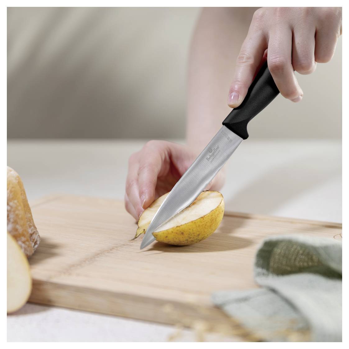 Hand slicing a pear on a cutting board with a kitchen knife.<br>