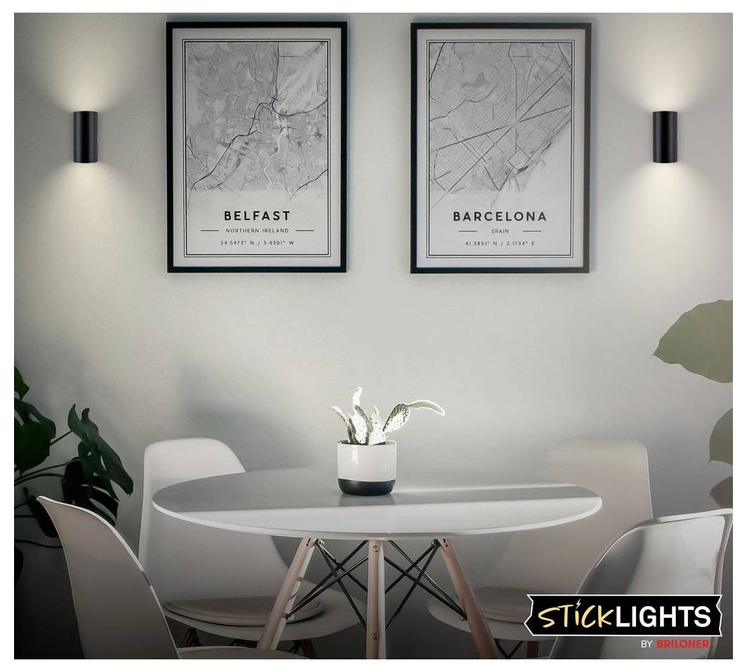 Modern dining nook with oval table, chairs, wall sconces, and framed city maps labeled 'Belfast' and 'Barcelona'.
