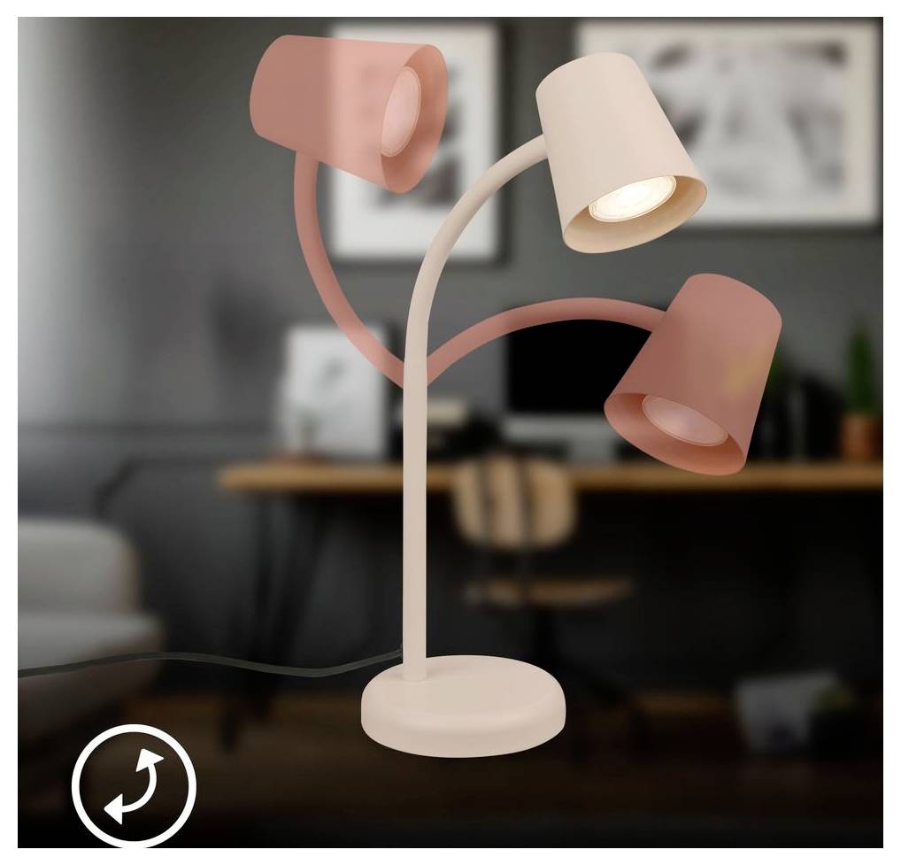 Pink three-head desk lamp on a round base, with adjustable shades and a lit central bulb, shown in a blurred home office.<br>