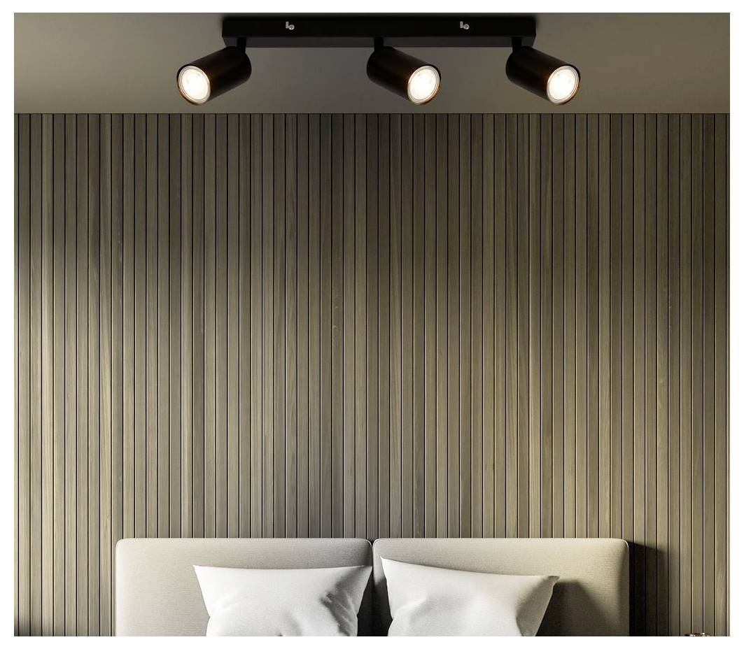 Minimal bedroom wall with vertical slat paneling and three ceiling spotlights above a bed with white pillows.