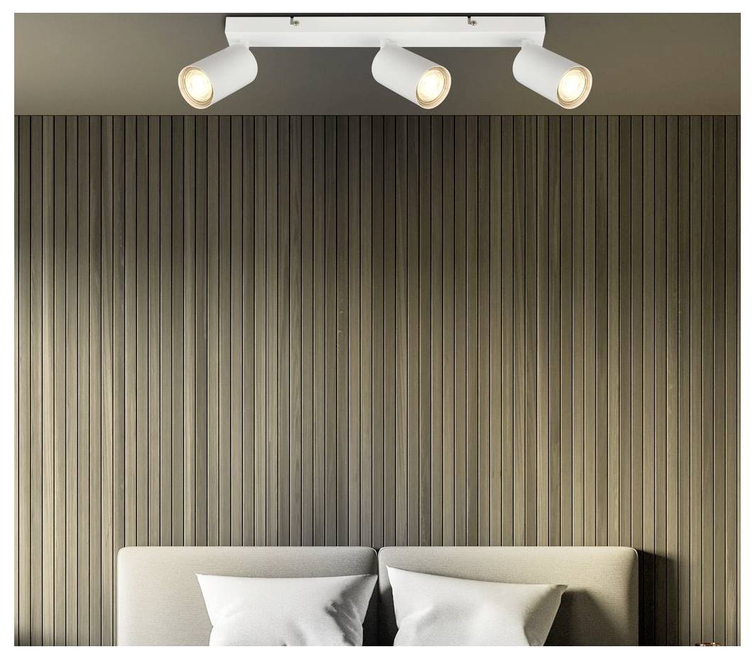 Bedroom with vertical wood wall panels, three ceiling spotlights, and the top of a bed with pillows below.