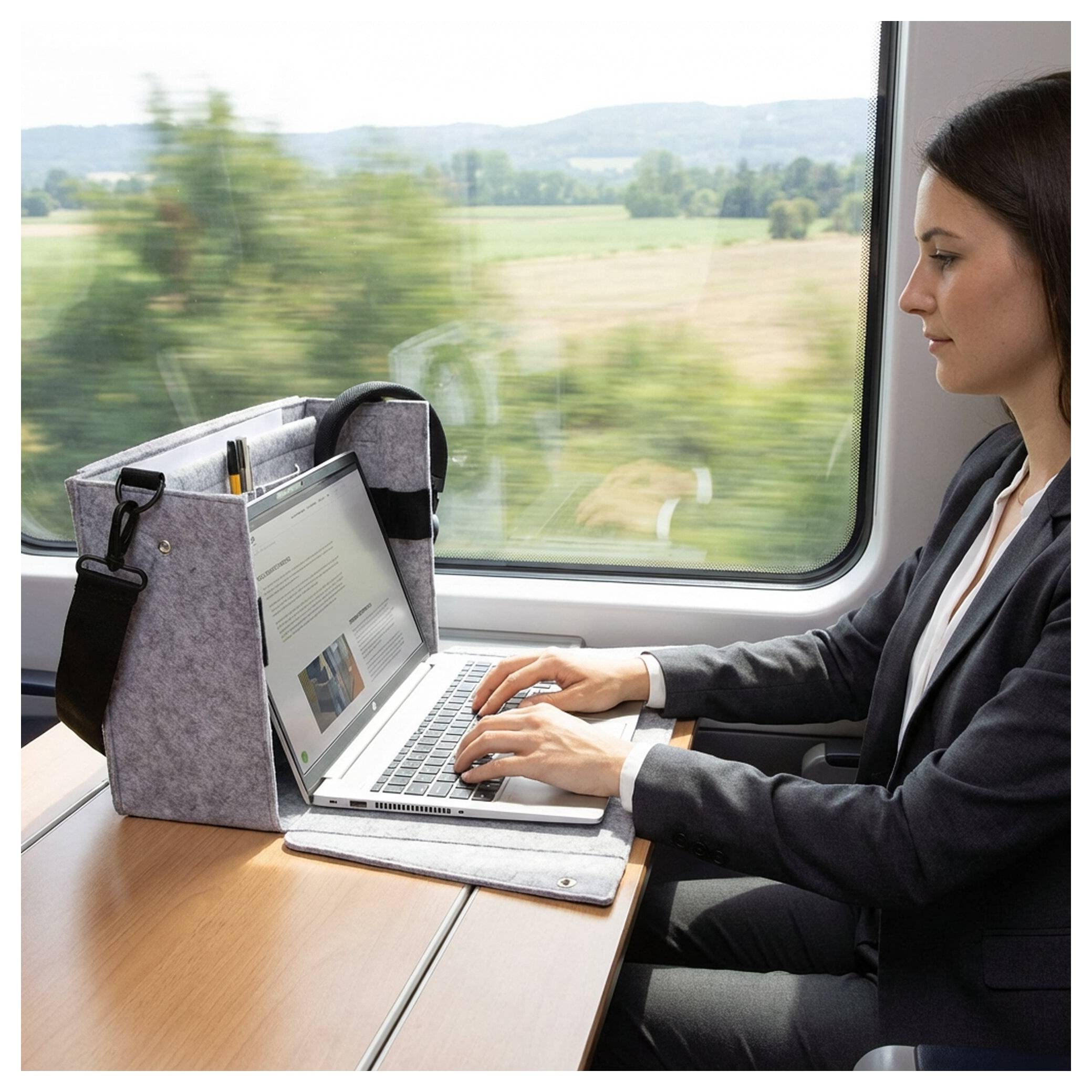 Woman working on a laptop at a train seat beside a window, with countryside blurred outside.