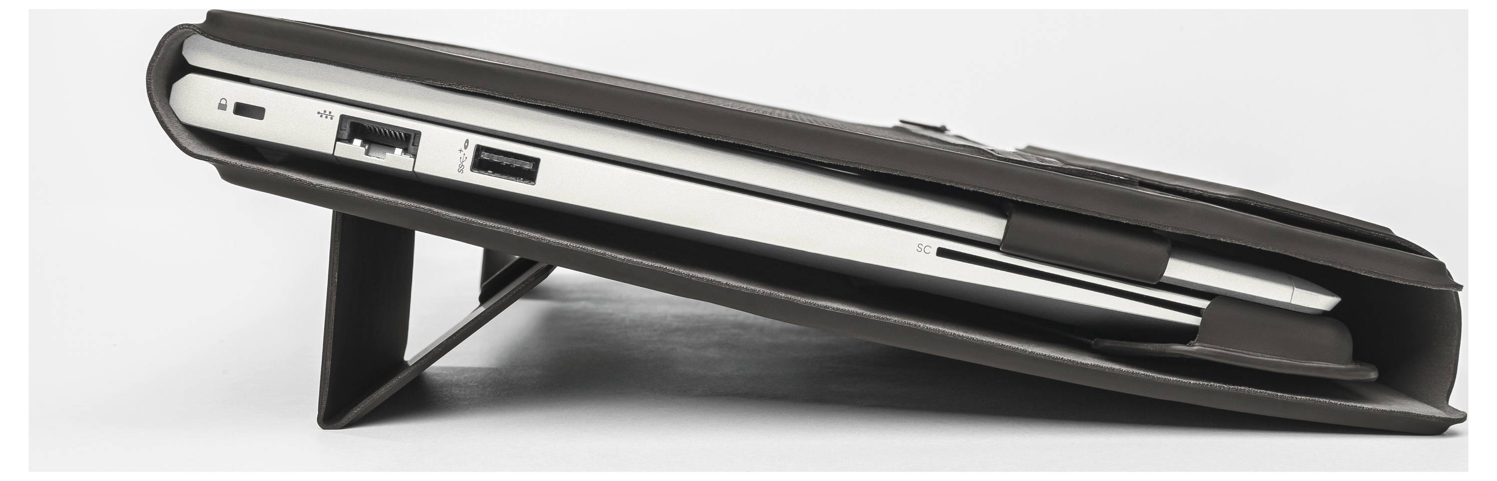 Closed laptop shown in side view, resting on a stand or wedge with ports visible along the edge.