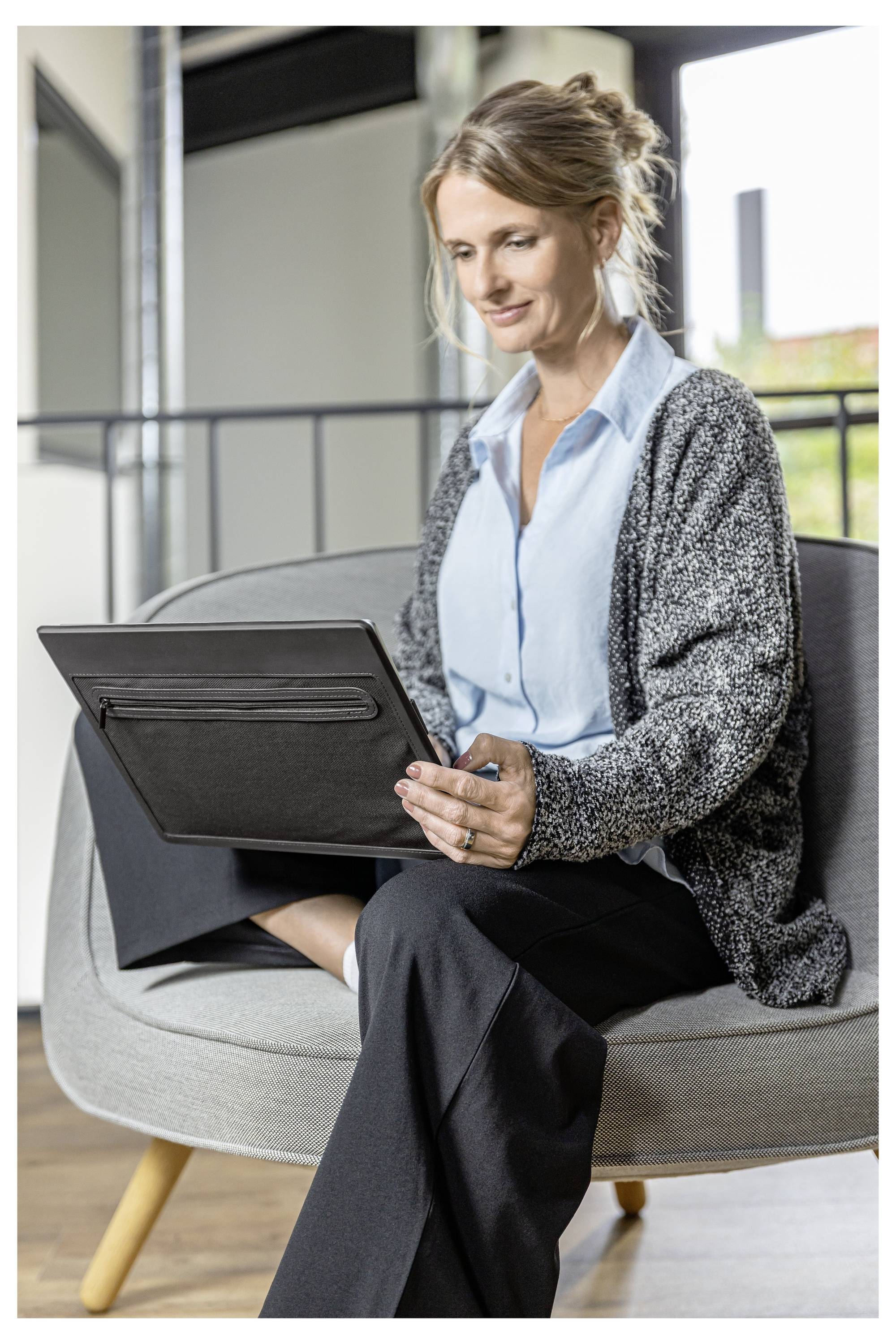 Woman sitting on a chair and using a tablet in a modern office or lounge area.
