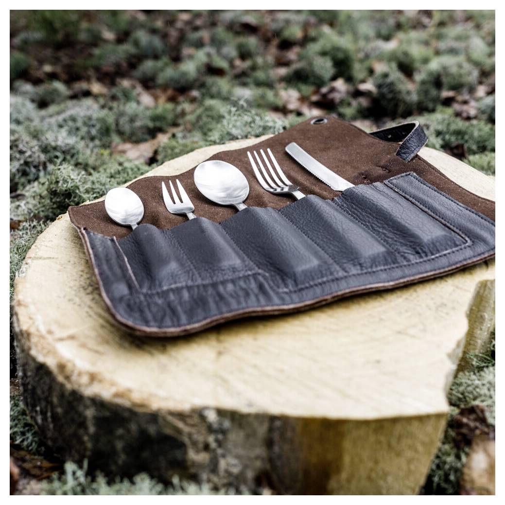 Set of silver utensils in a brown-and-black roll pouch resting on a cut tree stump outdoors.<br>