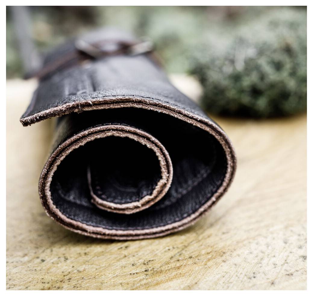Rolled black leather wristband or cuff on a wooden surface, shown in close-up.