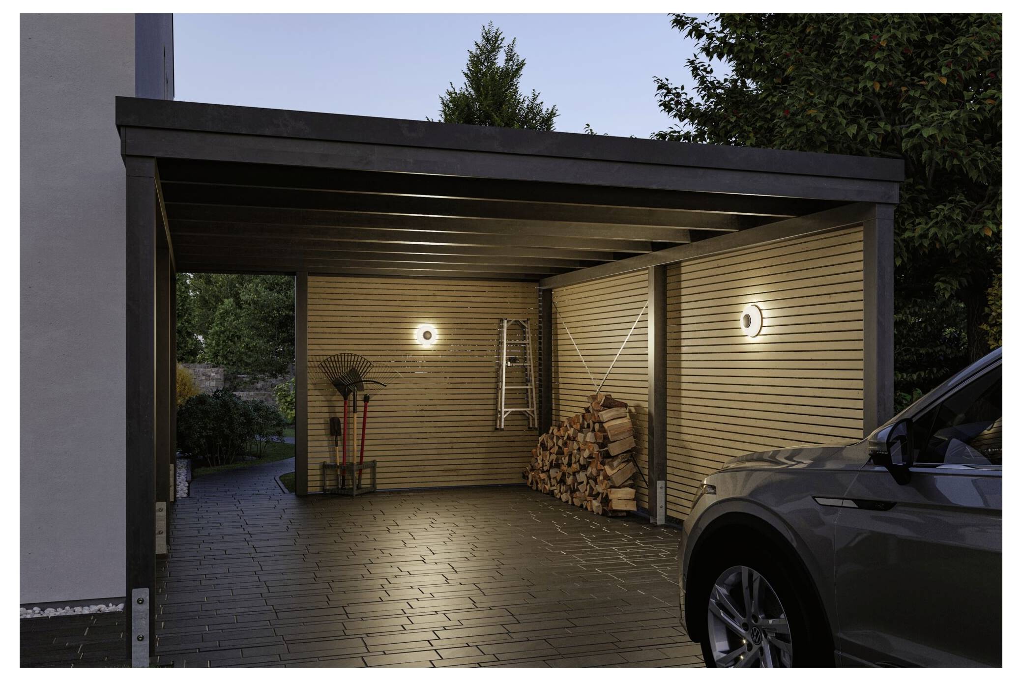 Covered carport at dusk with two wall lights, stacked firewood, garden tools, a ladder, and a parked SUV on the right.<br>