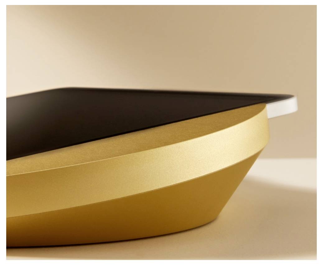 Close-up of a sleek, gold-and-black layered object with a curved metallic base on a neutral background.