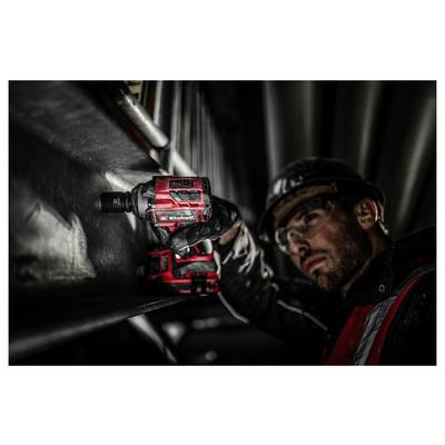 Worker using a red power drill inside a dark industrial space, leaning close to fasten or install equipment.