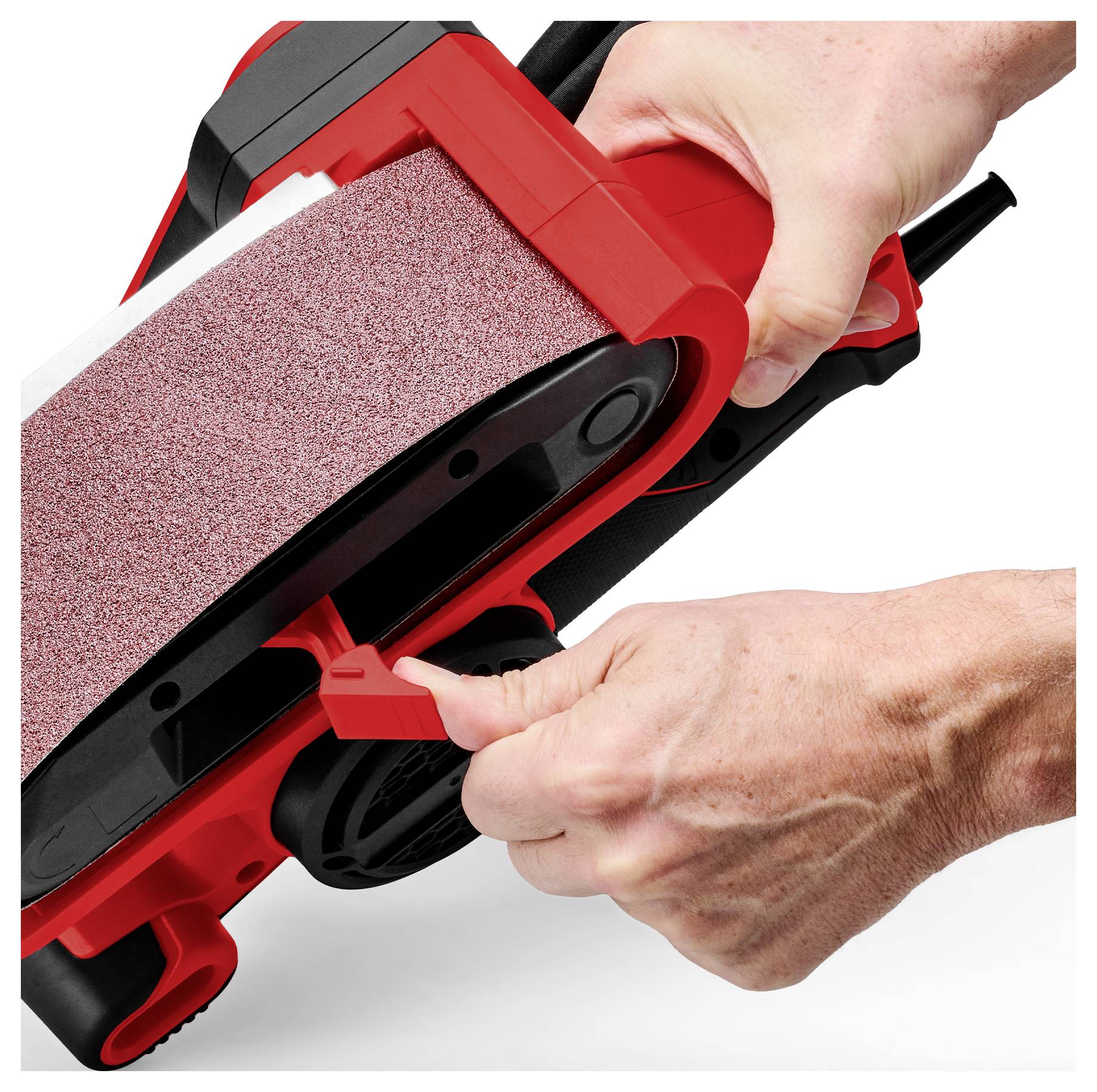 Close-up of hands tightening a red belt sander, showing the sanding belt and adjustment lever on a white background.<br>