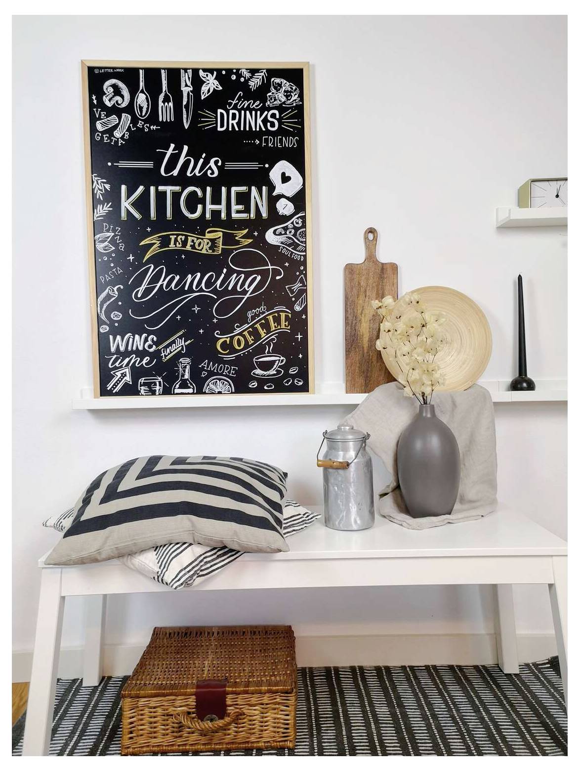 Stylish kitchen nook with a white bench, striped pillows, vase of dried flowers, wooden boards, and a chalkboard reading 'this KITCHEN is for dancing' and 'wine coffee'.