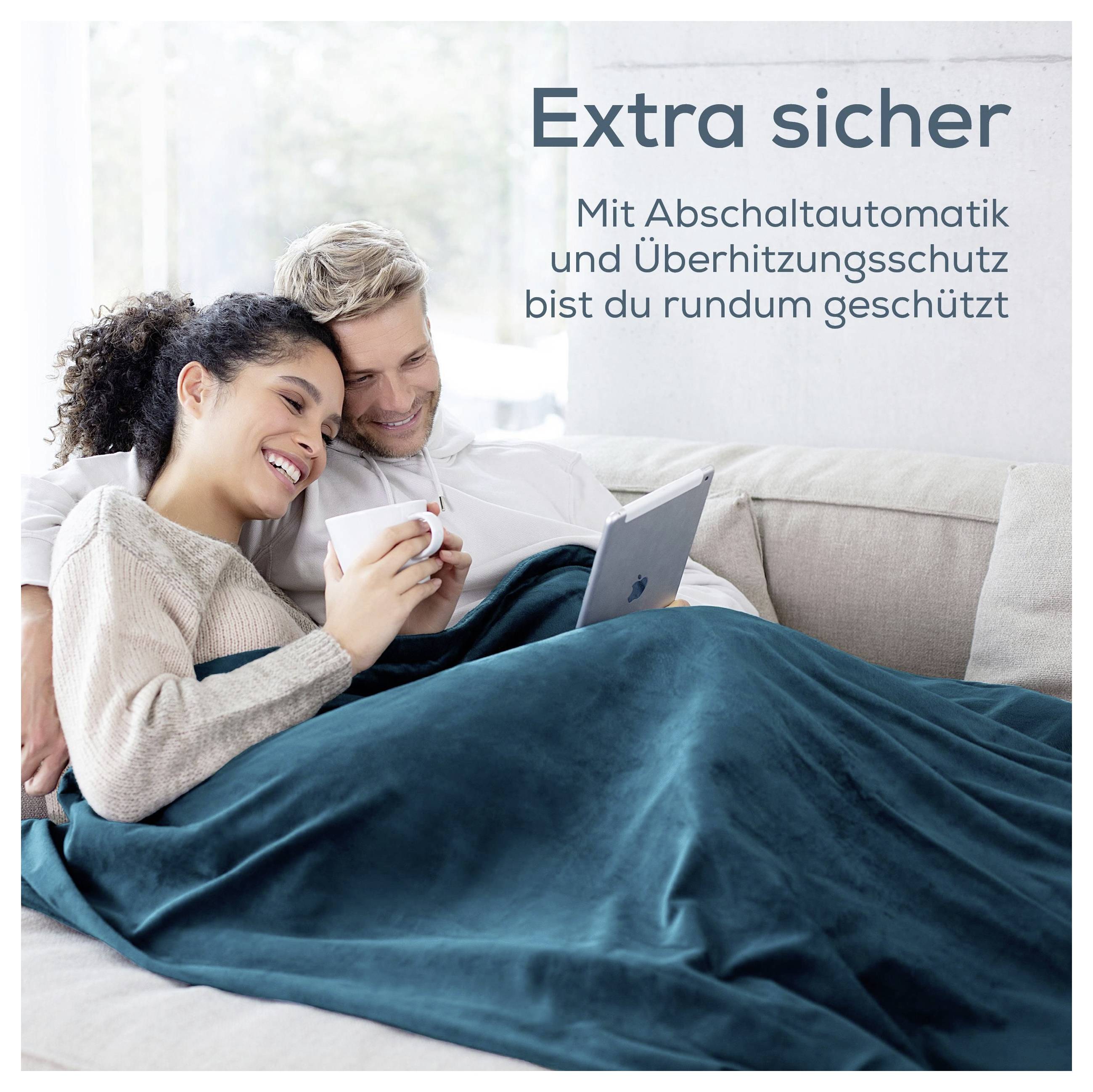 Couple cuddles with laptop under blanket on sofa; Text: 'Extra safe' and 'With auto-off function and overheat protection, you're completely protected'.