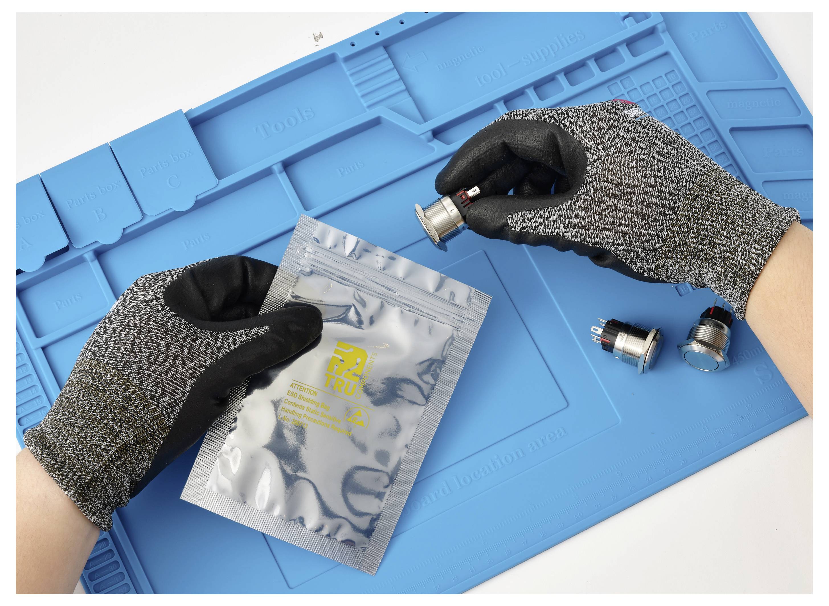 Gloved hands handle a silver resealable pouch and small metal vape parts on a blue work mat.<br>