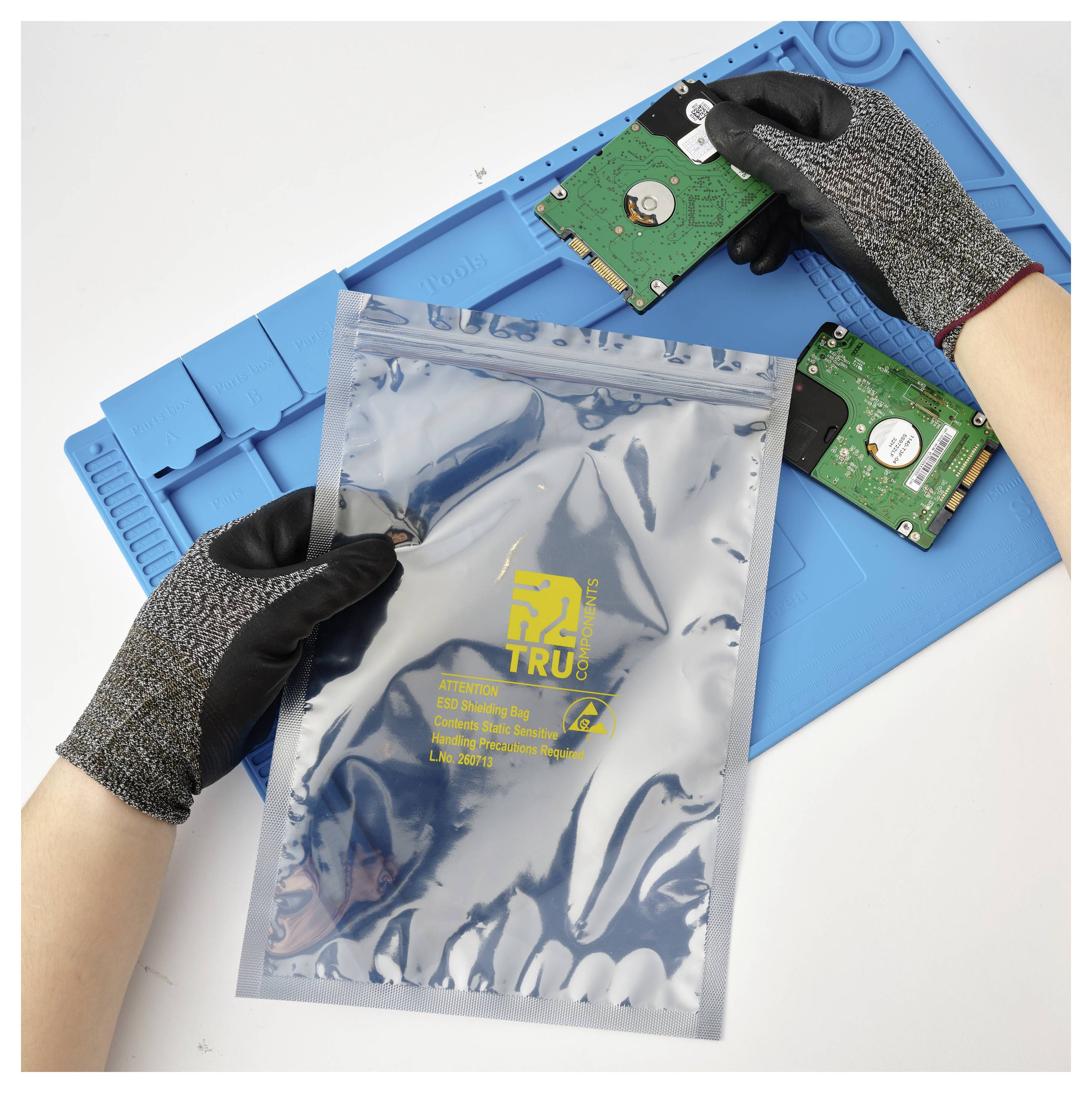 Gloved hands place a hard drive in an anti-static bag on a blue work mat, with two other hard drives nearby for safe computer part handling.