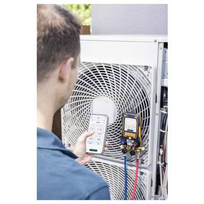 Technician checks an outdoor air conditioner unit with a smartphone app and digital gauges attached to the system.