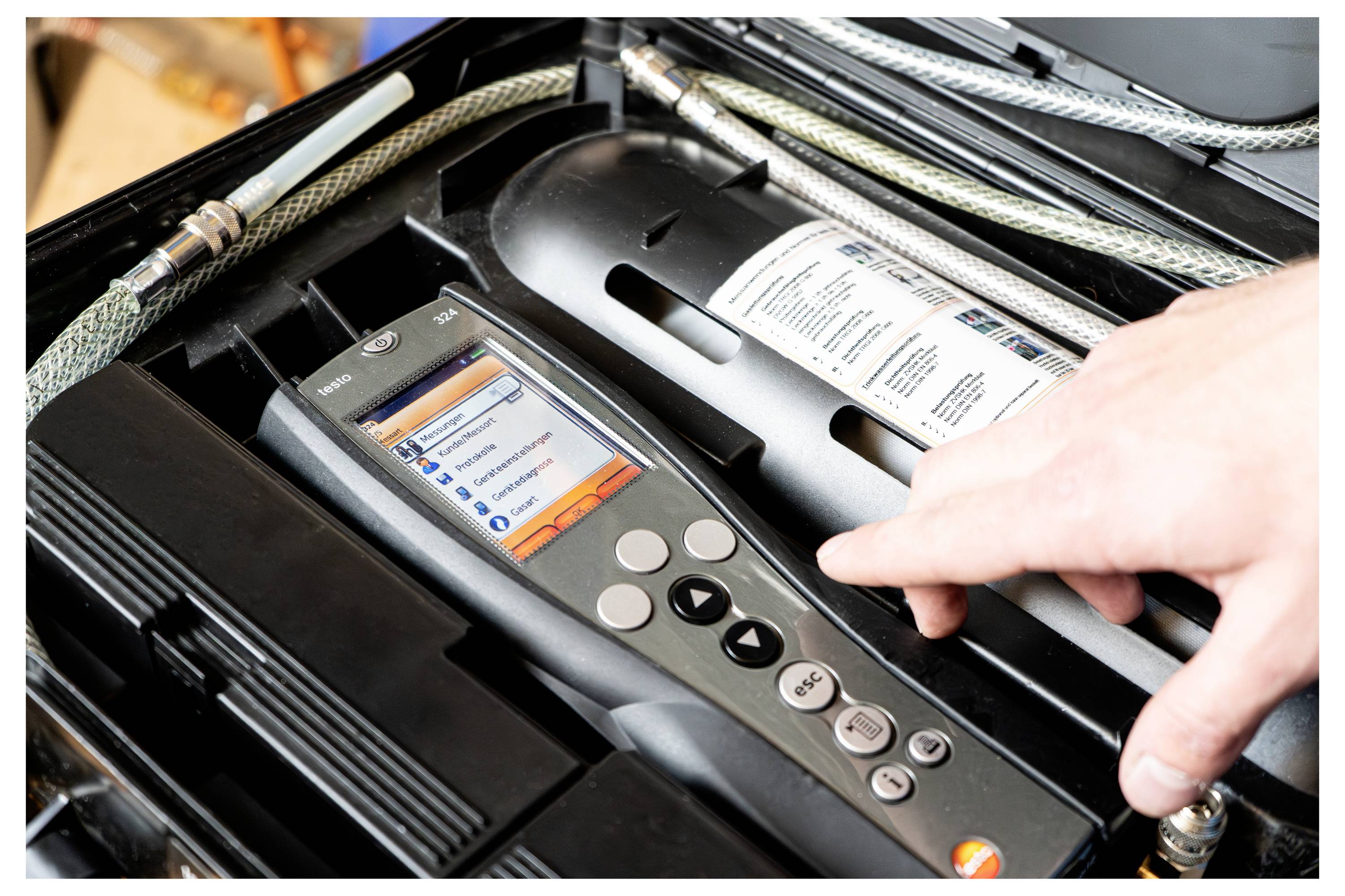 Hand adjusting a digital control panel inside an open machine or printer, with tubing and internal components visible.<br>