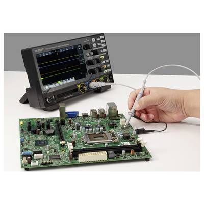 Hand using a test probe on a circuit board connected to an oscilloscope displaying signal traces, indicating electronic diagnostics.