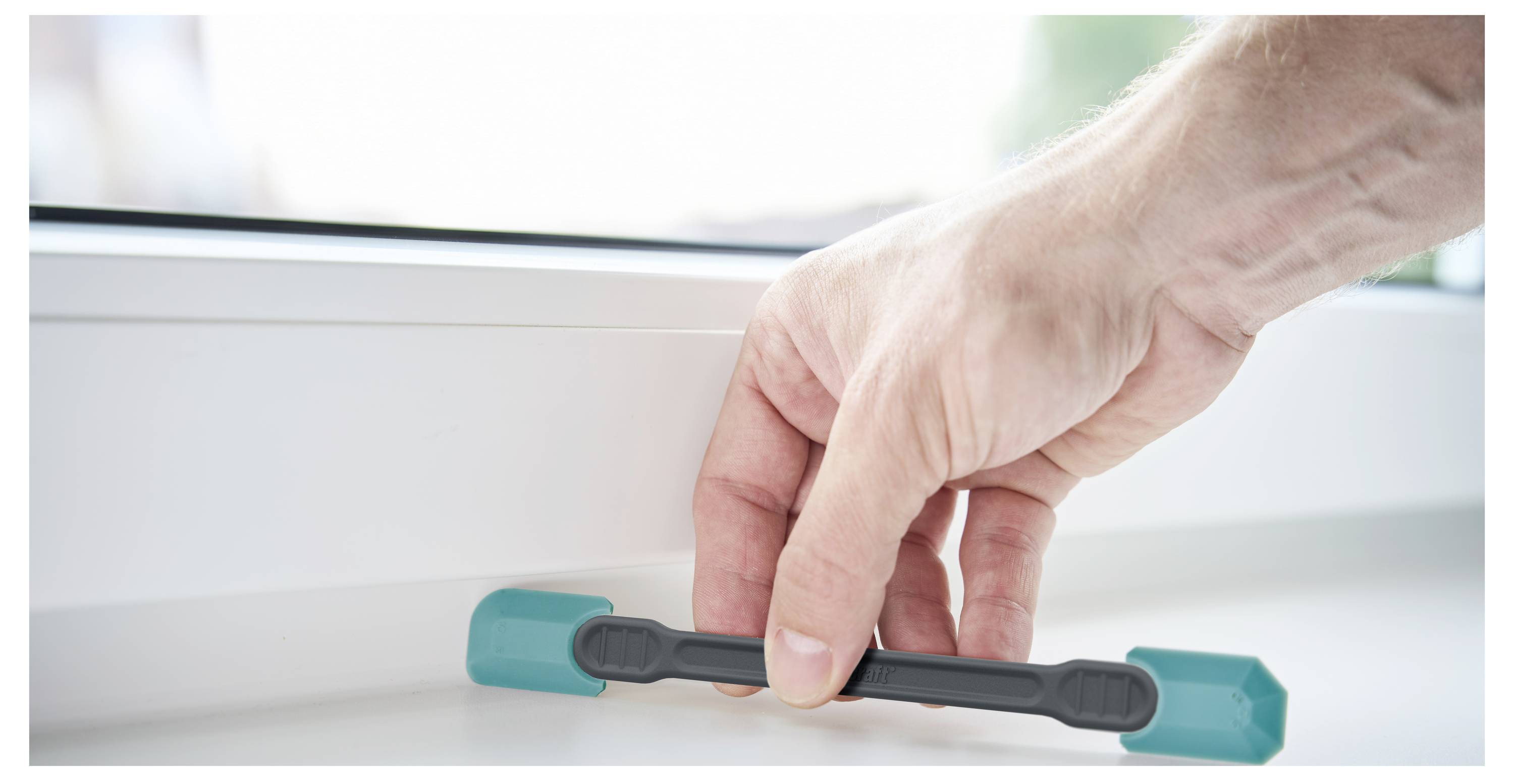 Hand turning a teal window latch on a white frame to open or close the window.<br>
