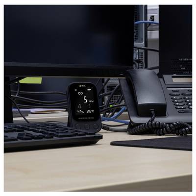 Small desk monitor displays office air quality readings: CO2 5 ppm, humidity 47%, and temperature 25°C beside a keyboard and phone.<br>