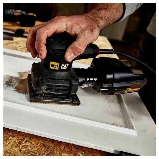 Hand using a CAT orbital sander to smooth a white painted cabinet door on a workbench.