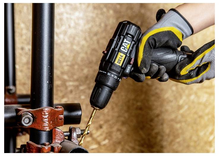 Gloved hands use a cordless drill to bore into a metal pipe clamp on black pipes.<br>