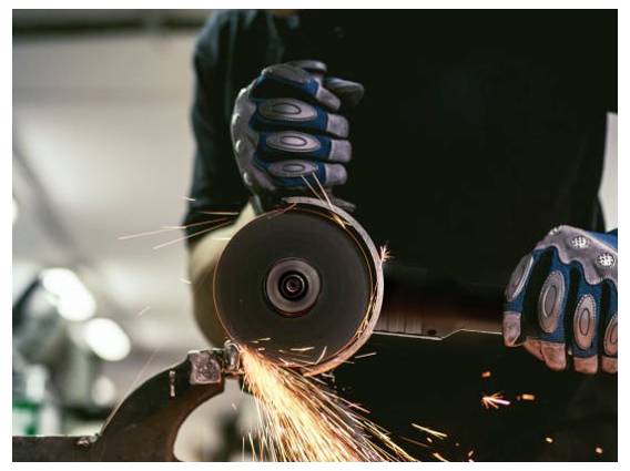 Person wearing gloves uses an angle grinder on metal, sending sparks flying.