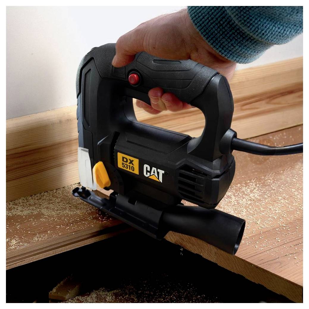 Handheld CAT jigsaw cutting a wooden board, with sawdust around the work area.