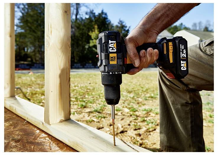 A person uses a CAT cordless drill to drive a screw into a wooden frame during construction.