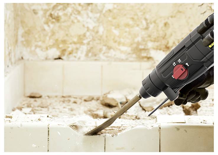 Close-up of a gloved worker using a power chisel to break away damaged plaster or tile from a wall.<br>