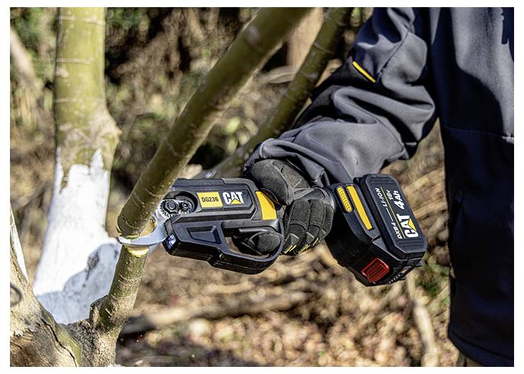 Gloved worker uses a cordless CAT pruning saw to cut a tree branch outdoors.<br>