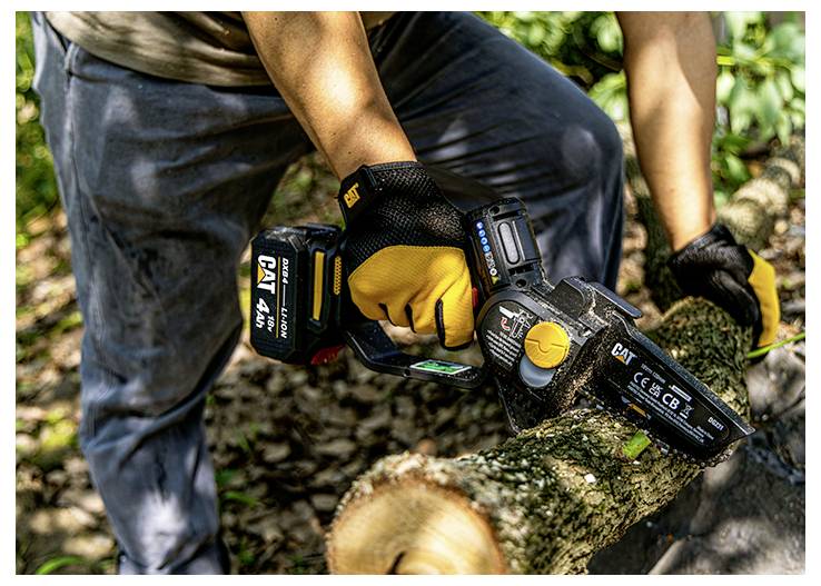 Person using a CAT cordless chainsaw to cut a fallen tree trunk outdoors in a wooded area.