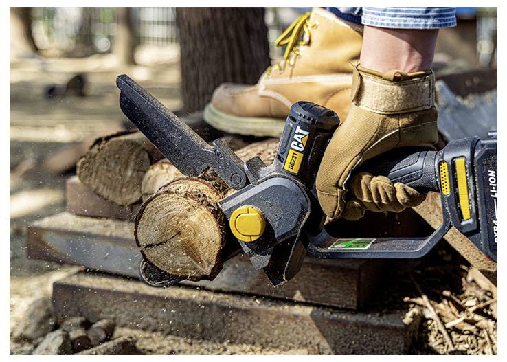 Gloved person using a battery-powered chainsaw to cut a log on stacked wood outdoors.